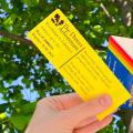 Hand holding Dawes Arboretum pass and library card against green leafy tree and blue sky