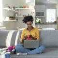 Woman sitting on a couch with a laptop and knitting