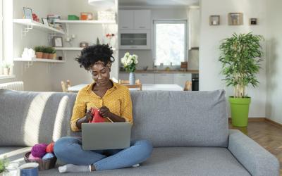 Woman sitting on a couch with a laptop and knitting